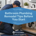 A plumber kneels beneath a bathroom vanity inspecting exposed sink plumbing and drain connections during a bathroom renovation.